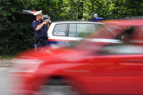 Polizist mit Radarpistole, roter Wagen rast vorbei