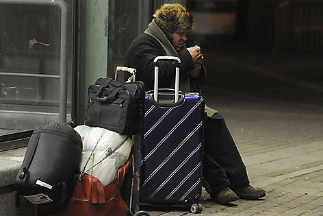 Obdachloser mit Koffer und Rucksack auf einer Bank