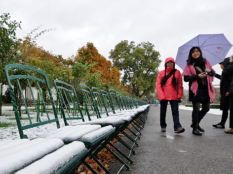 Schneebedeckte Sessel und Touristen im Wiener Burggarten
