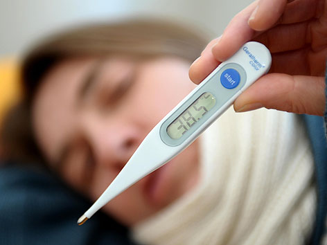 Frau misst mit einem digitalen Fieberthermometer die Körpertemperatur (gestellte Szene)
