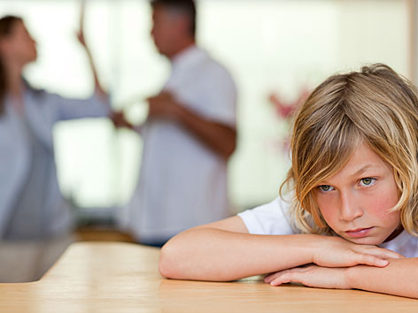 Ein Kind sieht traurig aus, im Hintergrund streiten sich die Eltern