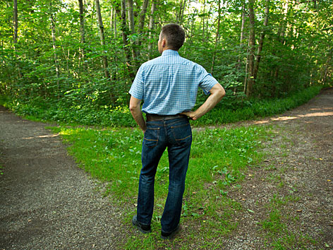 Ein Mann steht vor einer Weggabelung im Wald