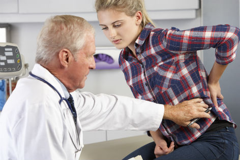 Arzt behandelt junge Frau mit Rückenschmerzen