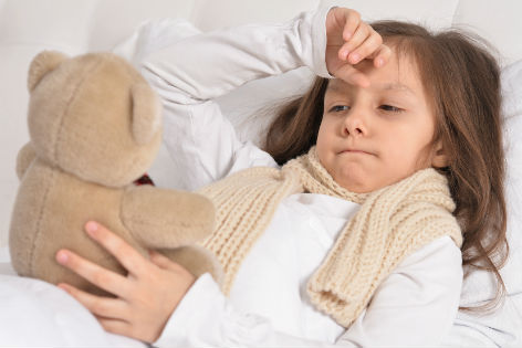 Krankes Kind liegt im Bett mit einem Teddybären