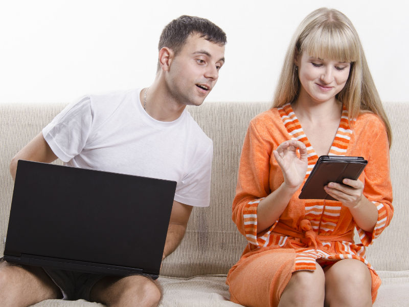 Mann und Frau sitzen mit Handy und Tablet auf Sofa